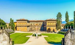 Il maestoso Palazzo Pitti si staglia contro un cielo azzurro, circondato da giardini lussureggianti e antiche scalinate.
