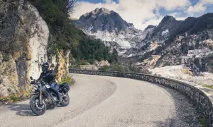 Motociclista su strada tortuosa con montagne di marmo sullo sfondo. Perfetto per itinerari moto Toscana 3 giorni.