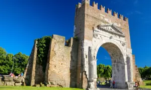 L'imponente arco augusto rimini, con la sua antica pietra e la torre in mattoni, si staglia contro un cielo azzurro.