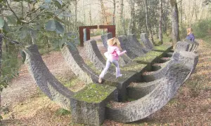 Bambini esplorano un **museo a cielo aperto in Toscana**, tra sculture in pietra e alberi secolari.
