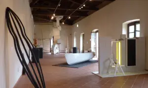 Interno del **mudac carrara** con sculture moderne, tra cui una grande forma nera appoggiata al muro e una barca bianca al centro.