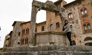 Donna sorride vicino a un antico pozzo a San Gimignano, con palazzi medievali sullo sfondo.