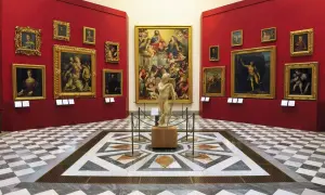 Sala con opere d'arte nei musei d'arte a Firenze. Statua di Cupido al centro, circondata da dipinti su pareti rosse.
