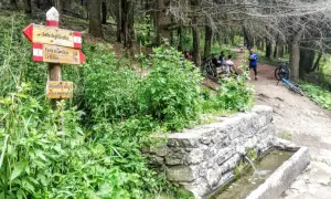 Segnavia per il trekking sul Monte Morello, con ciclisti che riposano vicino a una fontana.