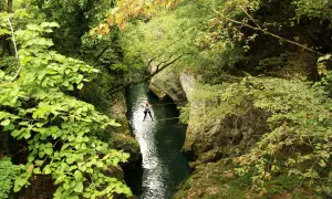 Persona cammina su un cavo teso sopra un fiume verde, un'avventura nella natura della **laguna blu Bagni di Lucca**.