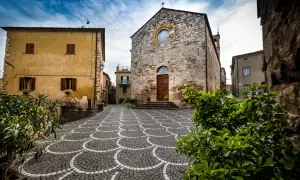 Piazza con pavimentazione a ventaglio, chiesa in pietra e case gialle, tipici borghi vicino Marina di Bibbona.