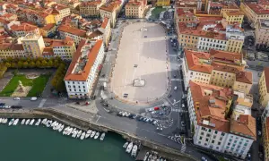 Vista aerea della piazza della Repubblica a Livorno, con edifici storici, un monumento centrale e barche ormeggiate nel canale.