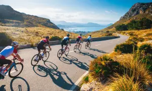 Ciclisti su strada panoramica, ideali per itinerari bici 3 giorni. Paesaggio montuoso e mare sullo sfondo.