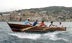 Equipaggio in gara nel palio marinaro argentario, vogando all'unisono con la città sullo sfondo.