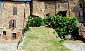 Antico borgo di Monteleone di Roncofreddo, con case in pietra e mattoni, finestre con persiane e un prato verde.