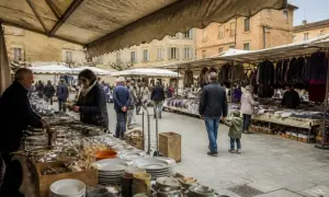 Gente al montepulciano markt, tra bancarelle di abiti e stoviglie, in una piazza storica.