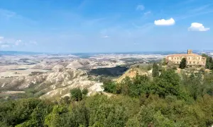 Panoramica delle balze di Volterra, con un antico palazzo in pietra su una collina e dolci colline ondulate all'orizzonte sotto un cielo azzurro.