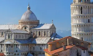 Pisa cosa vedere: il Duomo e la Torre Pendente, capolavori romanici che svettano nel cielo azzurro, con le montagne sullo sfondo.