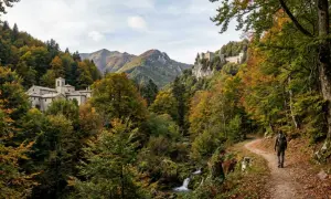 Un escursionista percorre un sentiero tra le Foreste Casentinesi in autunno, con un monastero e un eremo sullo sfondo.