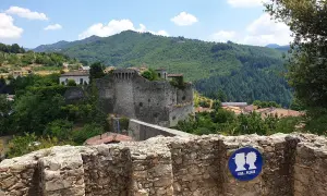 La rocca di Castiglione domina un borgo tra colline verdi. Un cartello invita a baciarsi.