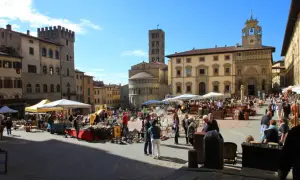 Piazza gremita per l'Arezzo antique market, tra bancarelle di antiquariato e palazzi storici sotto un cielo azzurro.