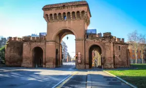 Le imponenti porte di Bologna, con i loro archi in mattoni rossi, accolgono i visitatori sotto un cielo azzurro.