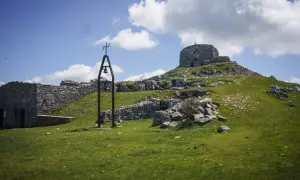 Rovine di pietra e una campana sul **monte Labbro**, sotto un cielo azzurro con nuvole bianche.