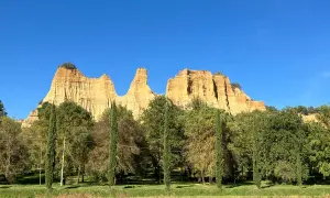 Le maestose balze del Valdarno si stagliano contro un cielo azzurro, circondate da una rigogliosa vegetazione e cipressi slanciati.