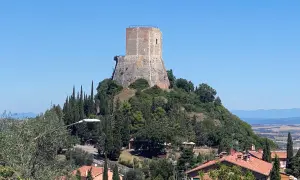 La rocca di Tentennano domina il paesaggio collinare toscano, circondata da cipressi e case con tetti rossi.
