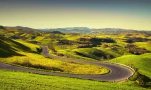 Strada volterrana serpeggia tra dolci colline verdi, un invito a esplorare paesaggi mozzafiato sotto un cielo limpido.