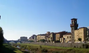 Pescia: cosa vedere? Un fiume serpeggia tra edifici storici e una torre imponente, sotto un cielo azzurro.