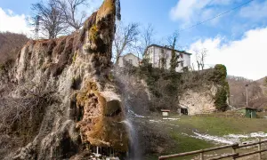 Cascata calcarea presso le grotte di Labante, con case in collina e cielo azzurro.
