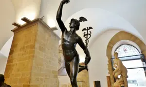 Mercurio in bronzo, un'opera che ricorda la grazia del David di Donatello. La statua, con il suo elmo alato, si staglia contro un soffitto ad arco.