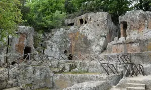 Antiche tombe scavate nella roccia, parte di siti etruschi, con sentieri e recinzioni in legno.