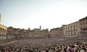 Folla immensa in Piazza del Campo a Siena, in attesa di sapere quand'è il Palio. Edifici storici e cielo terso.