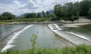Il **parco fluviale del Serchio** offre uno spettacolo di acqua che scorre su dighe naturali, circondato da verdi colline e alberi rigogliosi sotto un cielo nuvoloso.
