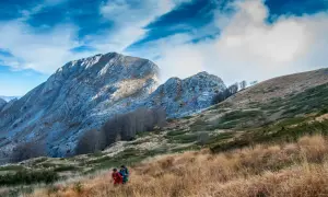 Due escursionisti attraversano un prato dorato, con le maestose Alpi Apuane sullo sfondo, un'esperienza di trekking tra i più belli.