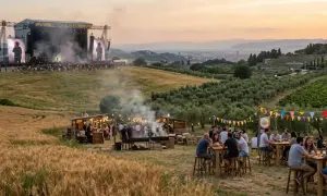 Un grande palco per il festival toscana con artisti e folla. In primo piano, bancarelle di cibo e persone che si godono l'atmosfera.