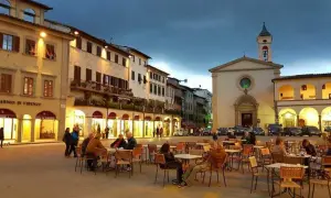Piazza serale con tavolini all'aperto e una chiesa, un'atmosfera incantevole nei borghi da visitare vicino a Figline Valdarno.