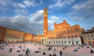 Piazza del Campo a Siena, un luogo iconico per il turismo, con il Palazzo Pubblico e la Torre del Mangia sotto un cielo nuvoloso.