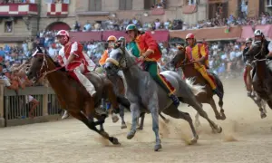 Cavalli e fantini in gara durante il Palio di Siena. La polvere si solleva mentre i cavalli corrono verso la vittoria.