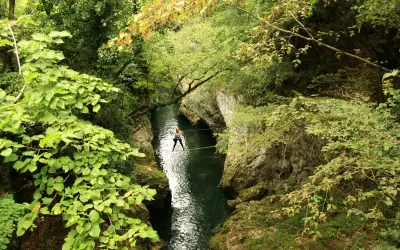 Persona cammina su un cavo teso sopra un fiume verde, un'avventura nella natura della **laguna blu Bagni di Lucca**.