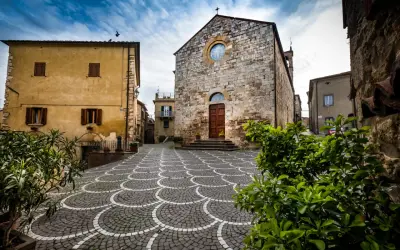 Piazza con pavimentazione a ventaglio, chiesa in pietra e case gialle, tipici borghi vicino Marina di Bibbona.