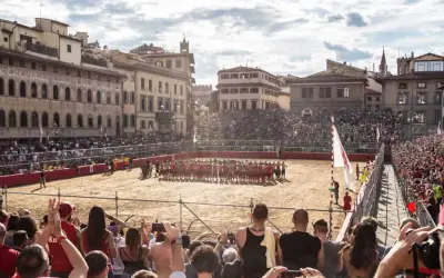 Un campo di sabbia a Firenze, gremito di spettatori, ospita un'intensa partita di calcio storico.
