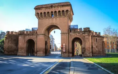 Le imponenti porte di Bologna, con i loro archi in mattoni rossi, accolgono i visitatori sotto un cielo azzurro.