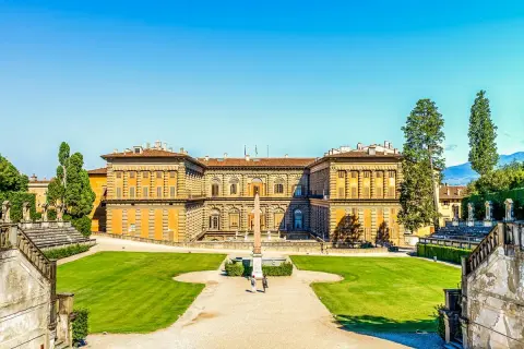 Il maestoso Palazzo Pitti si staglia contro un cielo azzurro, circondato da giardini lussureggianti e antiche scalinate.
