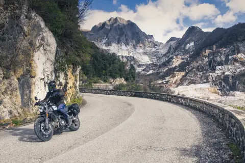 Motociclista su strada tortuosa con montagne di marmo sullo sfondo. Perfetto per itinerari moto Toscana 3 giorni.