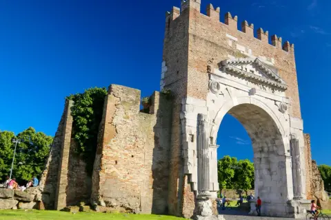 L'imponente arco augusto rimini, con la sua antica pietra e la torre in mattoni, si staglia contro un cielo azzurro.