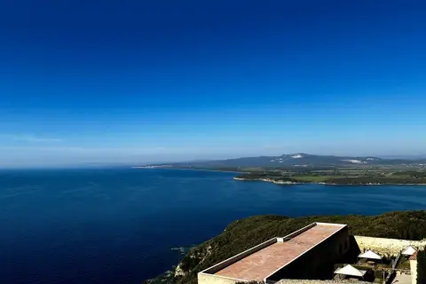 Vista panoramica sul mare blu intenso della Maremma, con colline verdi e un borgo antico. Perfetto per scoprire cosa vedere in Maremma.
