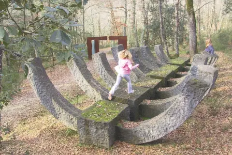 Bambini esplorano un **museo a cielo aperto in Toscana**, tra sculture in pietra e alberi secolari.