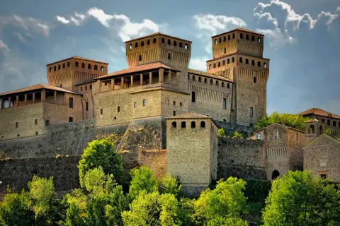 Rocche imponenti e torri medievali, tra i borghi vicino Parma, si stagliano contro un cielo nuvoloso, circondate da un verde lussureggiante.
