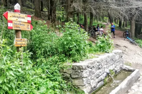 Segnavia per il trekking sul Monte Morello, con ciclisti che riposano vicino a una fontana.