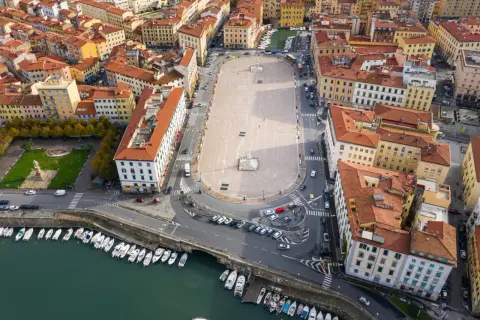 Vista aerea della piazza della Repubblica a Livorno, con edifici storici, un monumento centrale e barche ormeggiate nel canale.