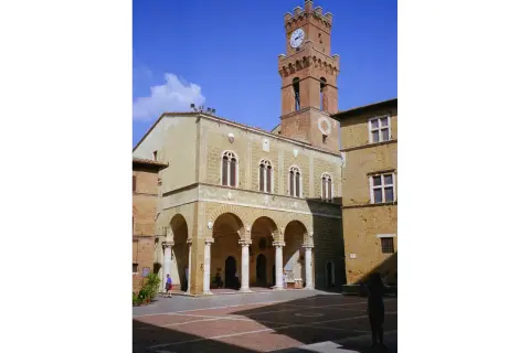 Il **Palazzo Comunale di Pienza** domina la piazza con la sua torre dell'orologio. Archi eleganti e finestre gotiche caratterizzano l'edificio.