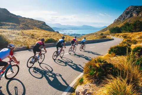 Ciclisti su strada panoramica, ideali per itinerari bici 3 giorni. Paesaggio montuoso e mare sullo sfondo.